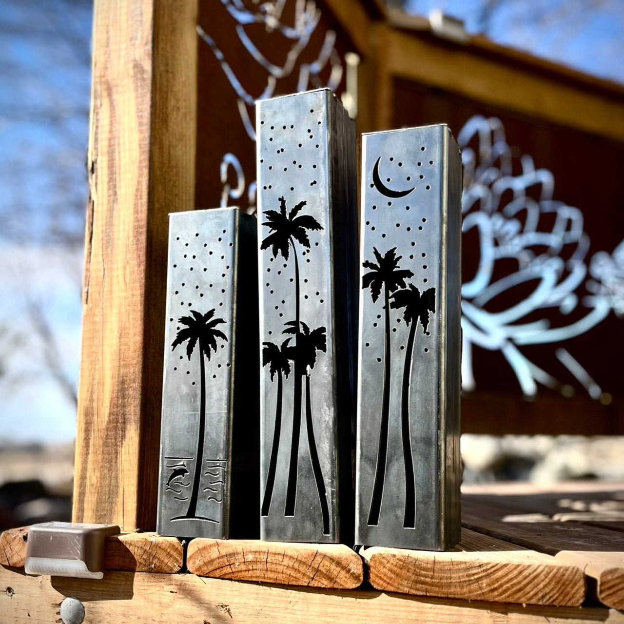 Outdoor garden columns with palm tree and moon designs on a wooden surface.