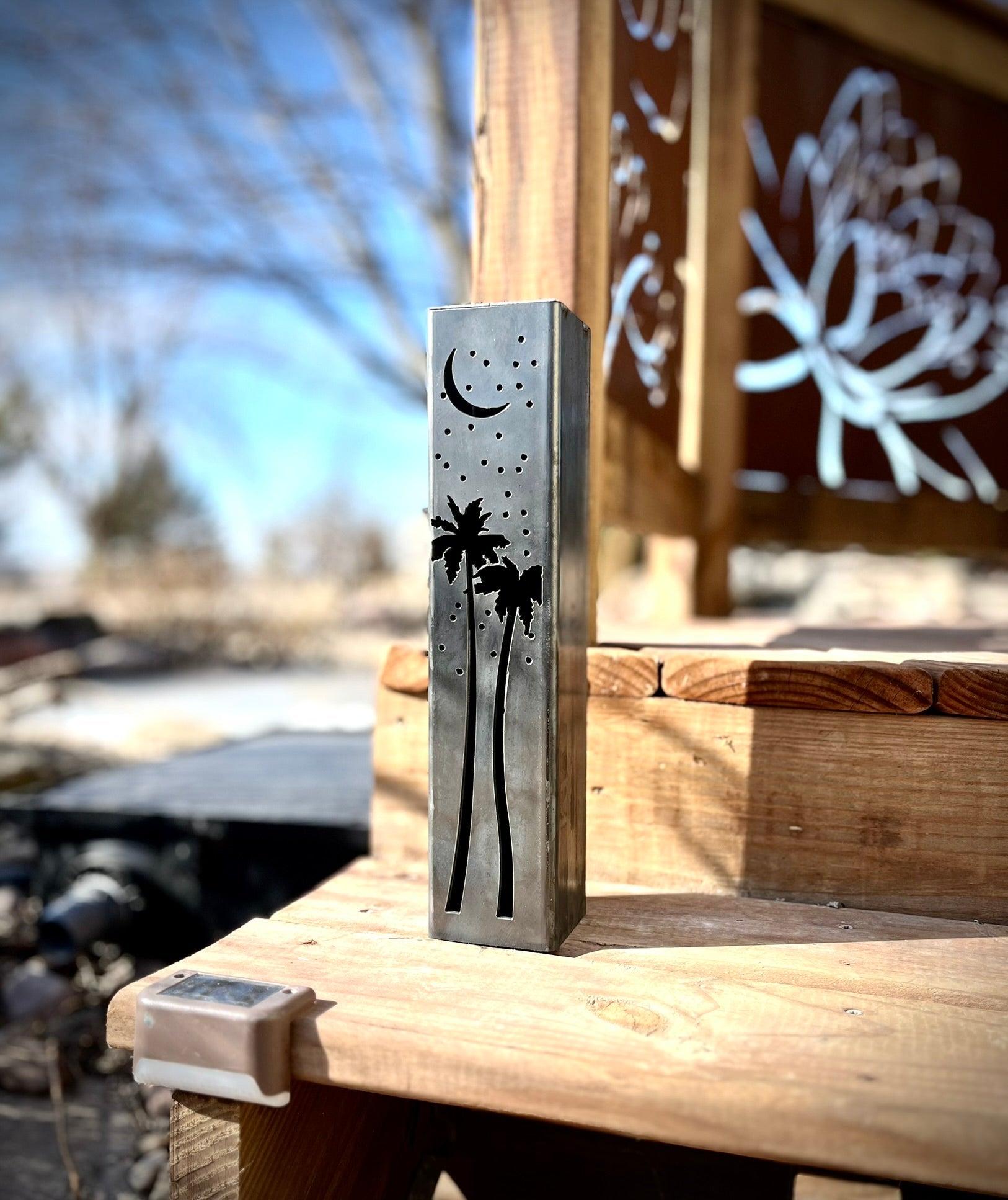 Outdoor garden column with palm tree and moon designs on a wooden surface.with palm tree and moon design on a wooden surface outdoors.
