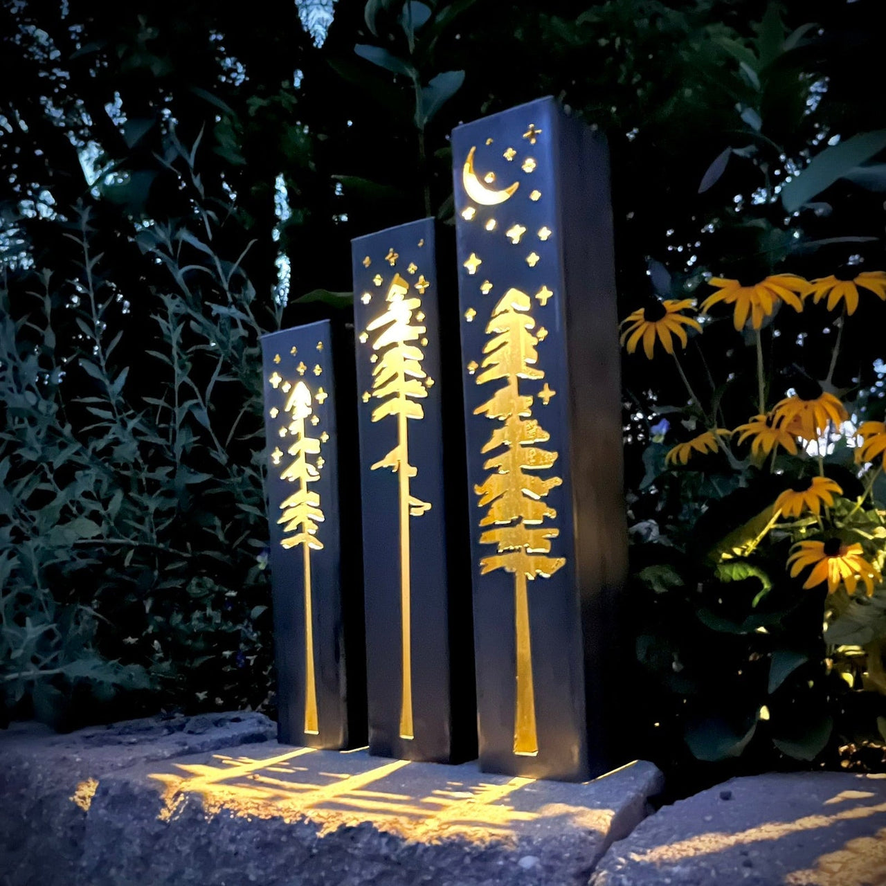 Decorative metal pillars with tree and moon designs in a garden setting.