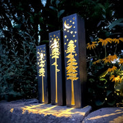 Decorative metal pillars with tree and moon designs in a garden setting.