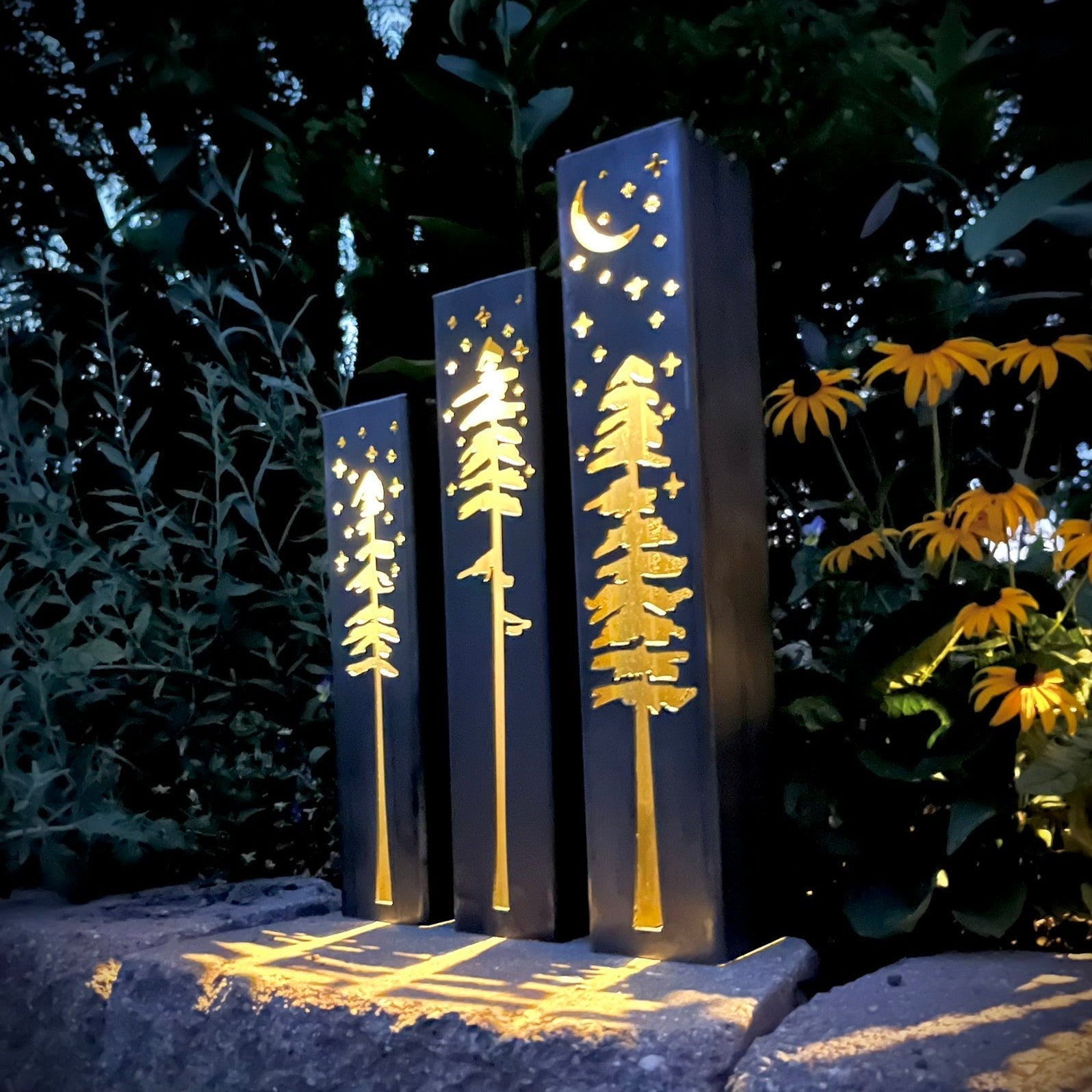 Decorative metal pillars with tree and moon designs in a garden setting.