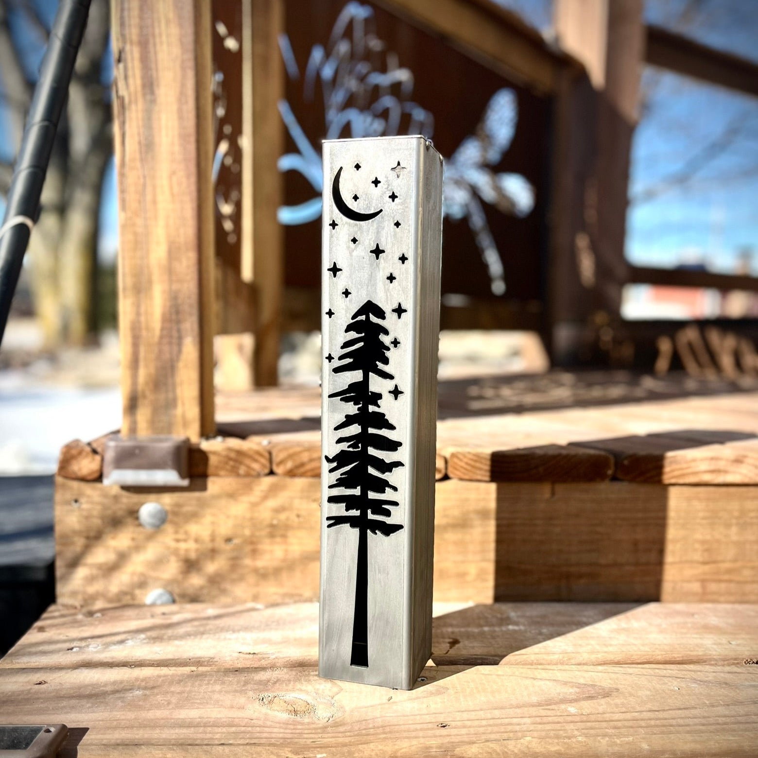 Metal pillar with tree and moon design on a wooden surface outdoors.