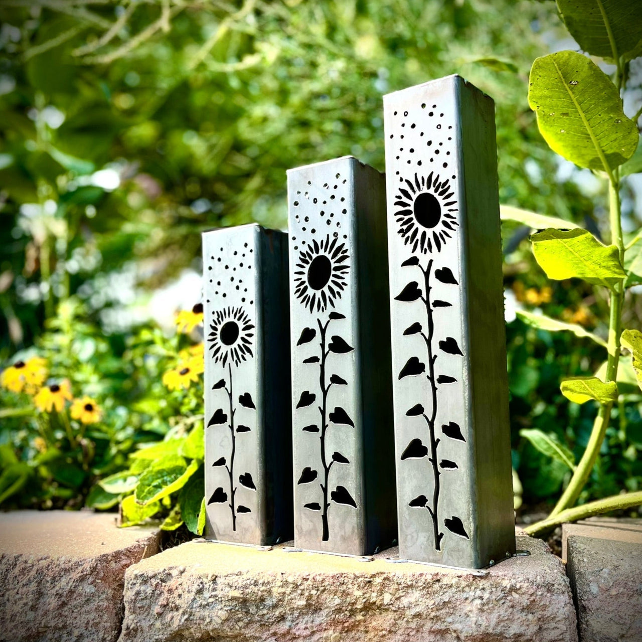 Three metal garden pillars  with sunflower designs on a stone ledge outdoors.